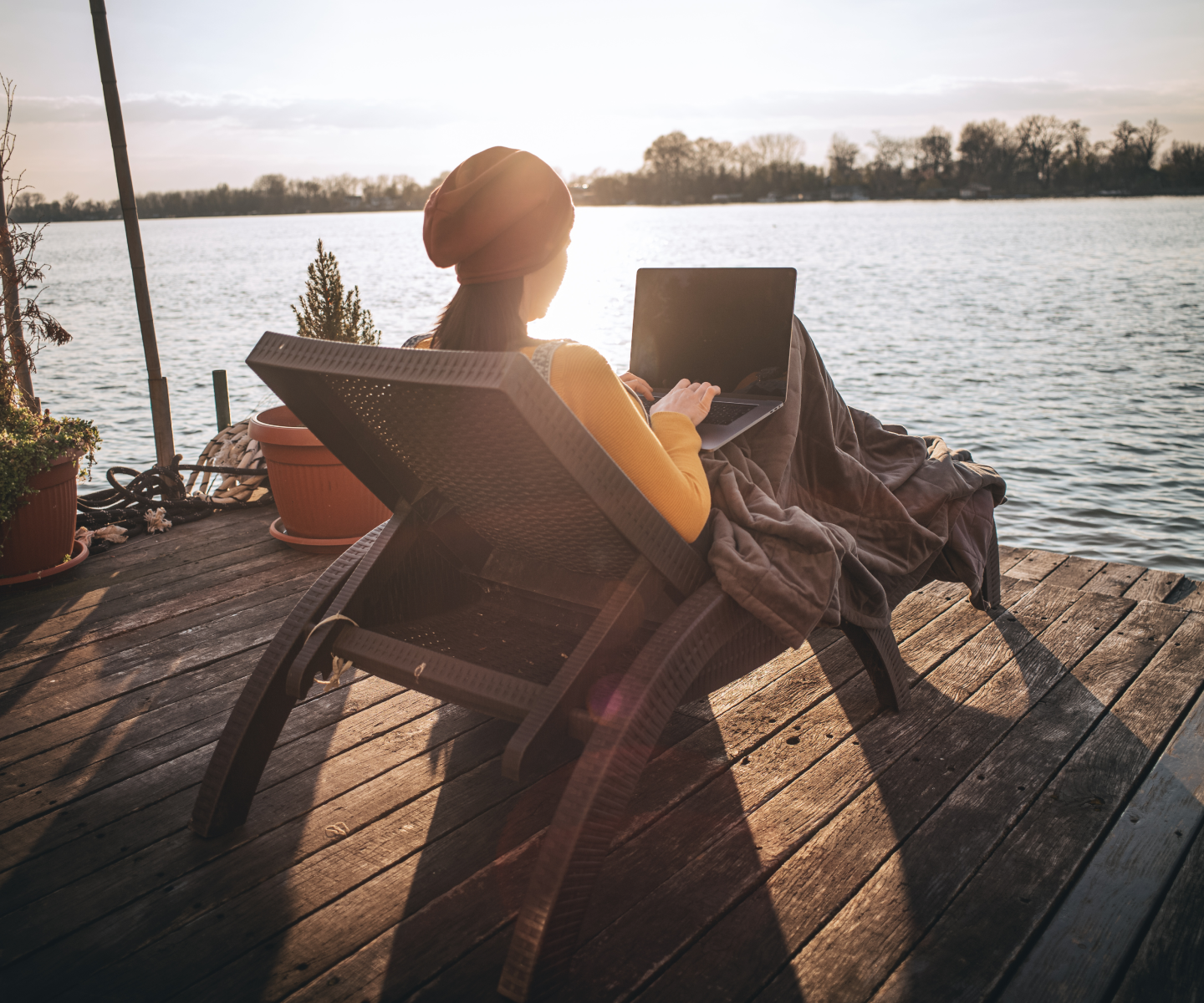 Woman sitting on a reclining chair on a dock next to the lake using a laptop.