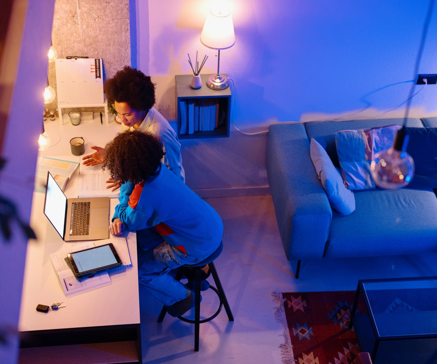 A family using a laptop and tablet with Frontier internet together for homework on a desk in a living room at night.